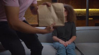 20 'li yaşlarda Afro-Amerikalı bir adam evdeki kanepede bekleyen kadına kese kağıdında yiyecek getiriyor. Aç milenyum insanları öğle yemeği yemeye hazır..