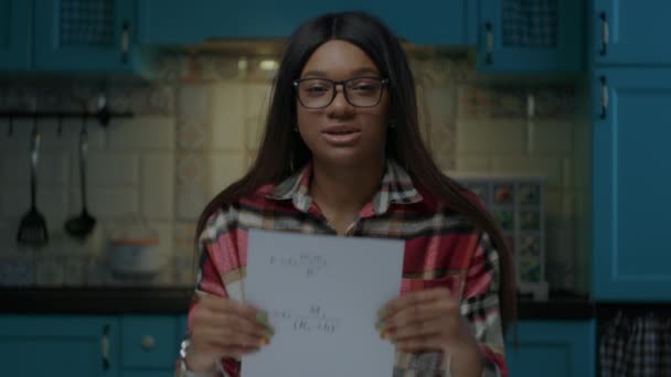 Afroamerikanischer Lehrer mit Brille spricht in die Kamera und zeigt ein Blatt Papier mit physikalischen Gleichungen. Webcam-Ansicht der Arbeit von zu Hause aus Online-Lehrer. Frau unterrichtet Physik. — Stockvideo