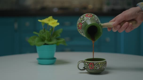 Mão feminina derramando bebida de café quente de panela de café de porcelana em xícara na mesa da cozinha em câmera lenta. — Vídeo de Stock