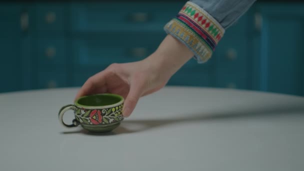 Vrouwelijke hand zetten porselein koffiekop en koffiepot op tafel in blauwe keuken interieur. — Stockvideo