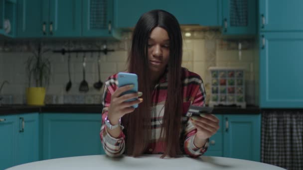 Genç, Afro-Amerikalı bir kadın online alışveriş için kredi kartıyla alışveriş yapıyor. İnternetteki cep telefonunda kadın banka kartı numarası yazıyor. Genç bayan internetten satın almaktan mutlu.. — Stok video