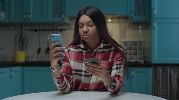 20s mujer afroamericana haciendo compra con tarjeta de crédito en línea. Número de tarjeta de débito de escritura femenina en el teléfono móvil. Mujer joven feliz de ir de compras en línea desde casa. — Vídeos de Stock