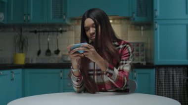 Genç Afrikalı Amerikalı kadın mutfakta cep telefonuyla video oyunu oynuyor. 20 'li yaşlarda cep telefonlu bir kadın online oyunlar oynuyor..