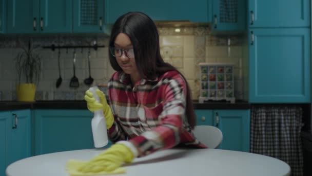 Millennial mulher afro-americana mesa de limpeza com agente de limpeza e pano usando luvas de borracha amarela na cozinha. — Vídeo de Stock