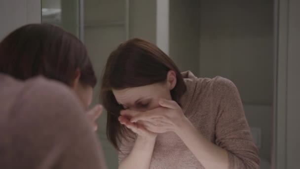 30 років жінка миє обличчя водою, дивлячись на дзеркало у ванній . — стокове відео