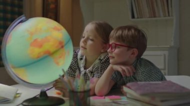 Öğrenci kız ve okul çocuğu ders kitaplarıyla Dünya küresi üzerinde çalışıyorlar. Kardeşler evde birlikte öğreniyor. Dünya gezegenini keşfeden çocuklar.
