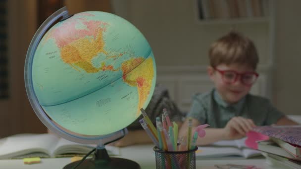 Dua anak belajar di rumah dengan bola bumi fokus pada meja. Gadis sekolah dan anak prasekolah belajar di rumah bersama-sama. — Stok Video