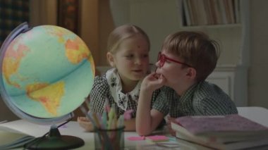 İki kardeş okul kitaplarıyla birlikte masada Dünya 'yı inceliyor. Liseli kız ve anaokulu çocuğu evde birlikte öğreniyorlar..