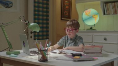 Anaokulu çocuğu evde online öğreniyor. Not defterine kalemle dizüstü bilgisayara bakan bir çocuk. Çocuklar için online ders.