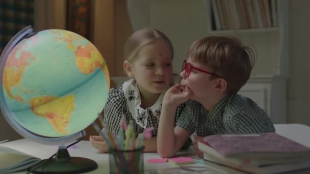 Dois irmãos a estudar o globo terrestre na mesa com livros escolares. Estudante e menino pré-escolar aprendendo em casa juntos. — Vídeo de Stock