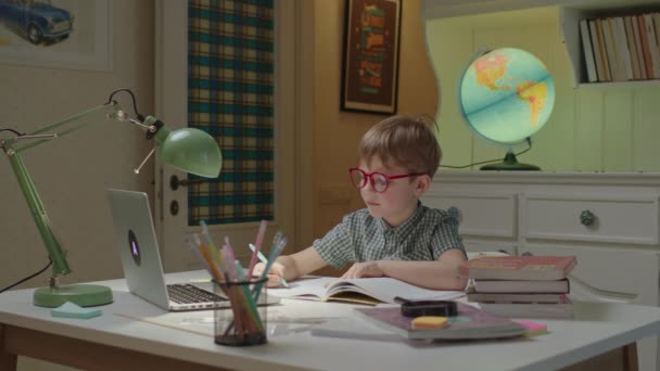 Elementary age boy writing down in notebook and showing to online teacher. Preschool child learning online at home. Online education and remote learning for kids — Stock Video