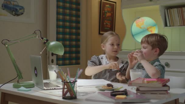Två syskon som roar sig med sötsaker som gör kakögon som håller kex i ansiktet. Roliga skolbarn som studerar online tillsammans. — Stockvideo