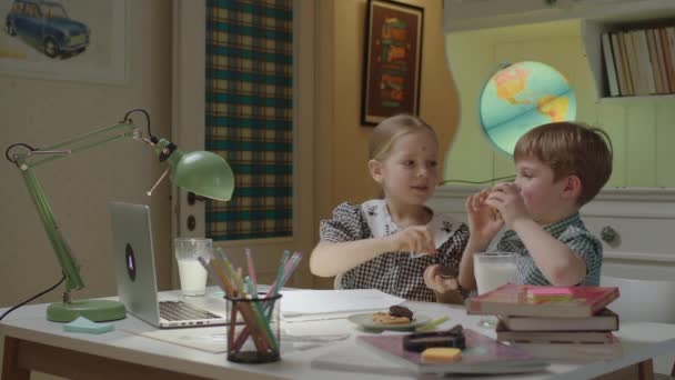 Two siblings having fun with sweets making cookies eyes holding biscuits by their faces. Funny school kids studying online together. — Stock Video