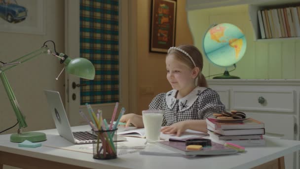 Schoolmeisje afmaken van webles en het hebben van online schoolvakantie met melk en koekjes. Hongerig schoolkind geniet van het eten van koekjes thuis. — Stockvideo