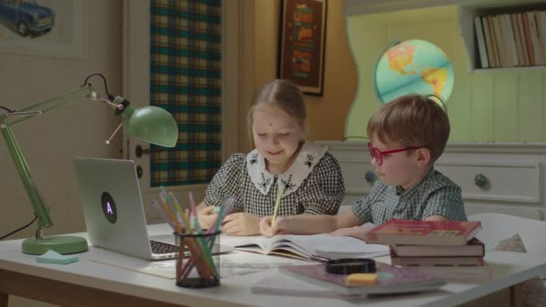 Dvě roztomilé děti studující on-line a ukazující hotové domácí úkoly pro online učitele na notebooku. Chlapec a dívka vzdálený učení doma. — Stock video