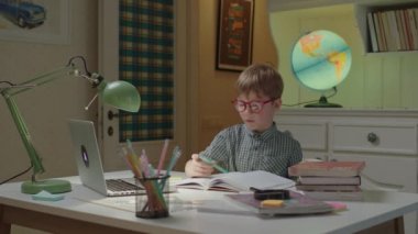 Anaokulu çocuğu deftere yazıyor ve online öğretmenle konuşuyor. Çocuk evde online öğreniyor. Çocuklar için internet eğitimi ve uzak mesafe öğrenimi.