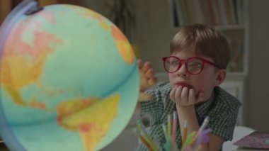 Dünya küresi üzerinde çalışan meraklı öğrenci. Anaokulu öğrencisi gözlüklü çocuk evde coğrafya öğreniyor. Şimşek dönen küre.