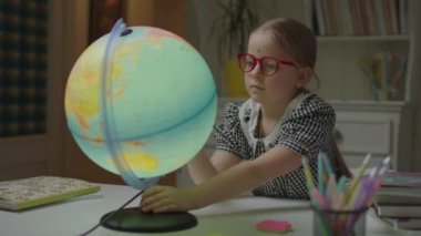 Evde coğrafya okuyan liseli kız masadaki Dünya küresini kullanıyor. Gözlük takan okul çocuğu evde tek başına öğreniyor. Şimşek dönen küre.