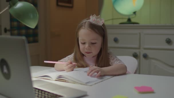 Sluiten van elementaire leeftijd meisje tekening met potlood en kijken naar laptop zitten alleen aan de tafel thuis. Online onderwijs voor jonge kinderen. — Stockvideo