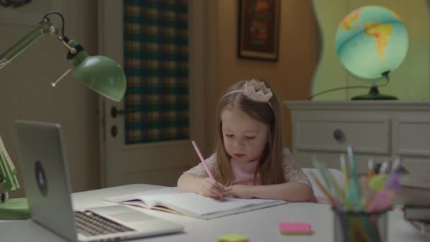 Elementary age girl drawing with pencil and looking at laptop sitting alone at the table at home. Online education for young kids. — Stock Video