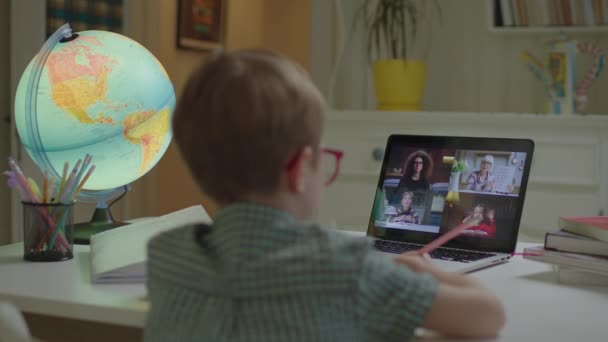 Kleuterjongen leren online met schoolleraar en leerlingen op laptop scherm. Een kind met een bril aan het bureau en een laptop. Afstandsonderwijs en thuisonderwijs. — Stockvideo