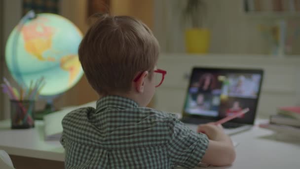 Förskolekillen har nätskolelektion med grupp lärare och elever på bärbar datorskärm. Barn i glasögon sitter vid skrivbordet i barnrum hemma och studerar online. — Stockvideo