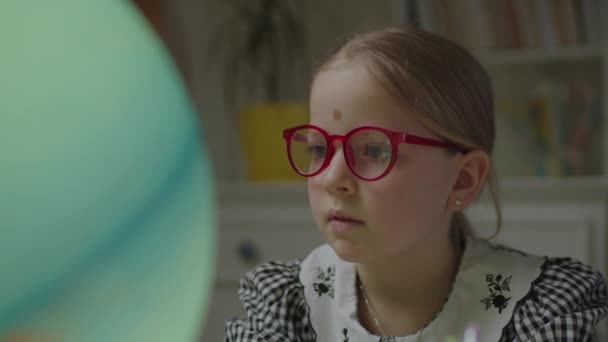 Close-up van nieuwsgierig schoolmeisje dat de aarde thuis bestudeert. Een kind met een bril die de aarde op aarde verkent. Thuis onderwijs. — Stockvideo
