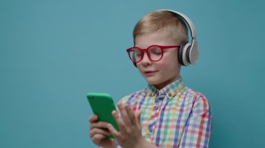 El ele tutuşan ve cep telefonunu birine veren bir çocuk. Mavi arka planda akıllı telefon uygulaması kullanan gözlüklü ve kulaklıklı genç bir çocuk..