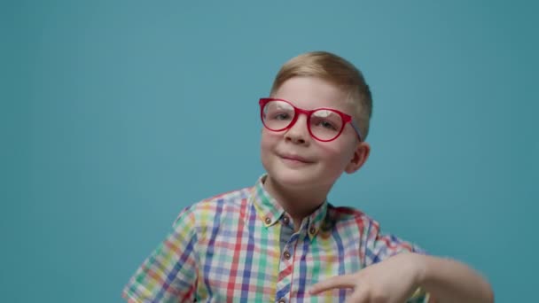 Veselé dítě tančící a dívající se na kameru na modrém pozadí ve zpomaleném filmu. Chlapec v brýlích legrační tanec. — Stock video