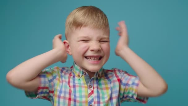 Glimlachende jongen sluit oren met handen en huilt NEE IK hoor je niet op een blauwe achtergrond staan. Draaiend kind met gesloten oren dat weigert te horen. — Stockvideo