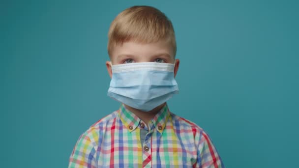 小孩戴着防护面具,用大拇指向上看蓝色背景的相机.对社会负责。遏制疾病的蔓延. — 图库视频影像