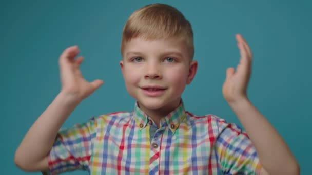 Kleuterschooljongen sluit oren met handen en schreeuwt NEE kijkend naar camera die op een blauwe achtergrond staat. Kind weigert iets te horen.. — Stockvideo