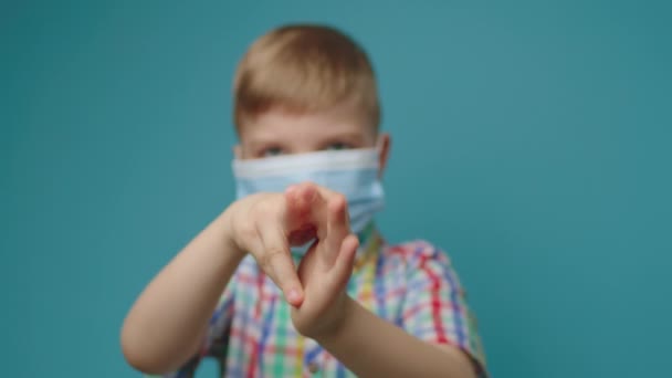 Kind draagt gezicht beschermende masker schoonmaak hand met ontsmettingsmiddel staan op blauwe achtergrond. Wees sociaal verantwoordelijk. Stop de verspreiding van ziekten. — Stockvideo