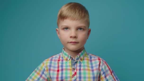 Menino pré-escolar assumindo máscara protetora facial em pé no fundo azul olhando para a câmera. Retrato de criança usando máscara facial. — Vídeo de Stock