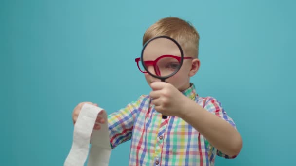 Jongen verkent winkelbon kijkend door vergrootglas. Verrast kind onderzoekt ontvangst winkel met loupe. — Stockvideo