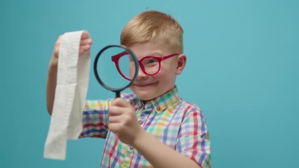 Vorschulkind mit Brille wundert sich über große Scheine oder Quittungen, die durch die Lupe betrachtet werden. Überraschtes Kind begutachtet Kassenbon mit Lupe. — Stockvideo