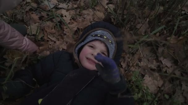 Děti si venku hrají v temném podzimním lese. Usmívající se chlapec si hraje s dívkou v zimních bundách. Dítě ležící na zemi. — Stock video