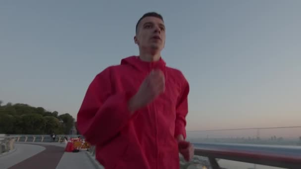 Hombre de 20 años con chaqueta deportiva corriendo por la calle temprano en la mañana. Ejercicio de entrenamiento al amanecer. Vida milenaria saludable. — Vídeos de Stock