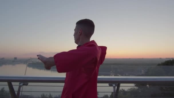 Hombre milenario en ropa deportiva calentándose antes de correr al amanecer. Ejercicios de entrenamiento deportivo por la mañana. — Vídeos de Stock