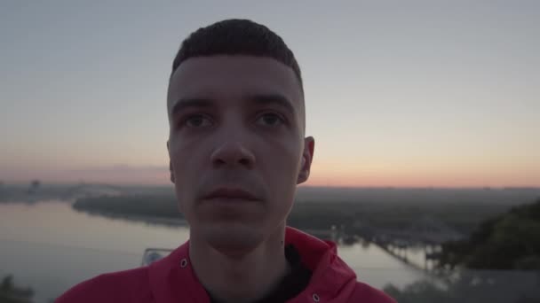 Portret van een duizendjarige man die bij zonsopgang aan de rivier staat. Vroege ochtend mensen sport training. — Stockvideo