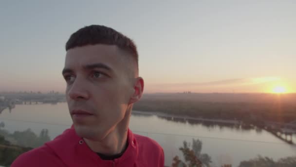 Hombre de 20 años en ropa deportiva calentándose antes de correr al amanecer. Ejercicios de entrenamiento deportivo por la mañana. — Vídeo de stock