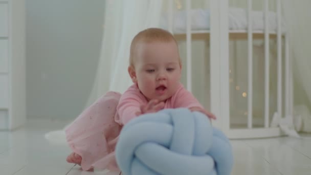 Bambino neonato in abito rosa seduto e giocare sul pavimento in camera dei bambini luminosi. Carino bambino di 10 mesi con grandi occhi blu. — Video Stock