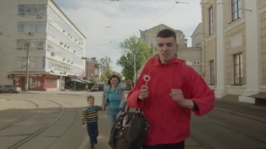 Male thief running with womans bag and kids lollipop on the street. Woman and boy catching up with bag thief. Mother and son running behind young adult man who stole bag and lollipop.