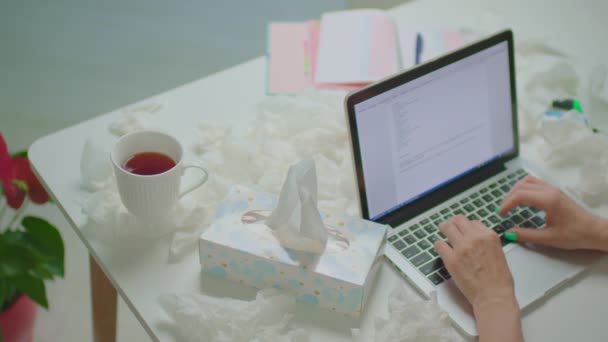 Sick woman working on laptop from home. Woman blows her nose with paper napkins and typing on laptop. Flu and other respiratory diseases at home. — Stock Video