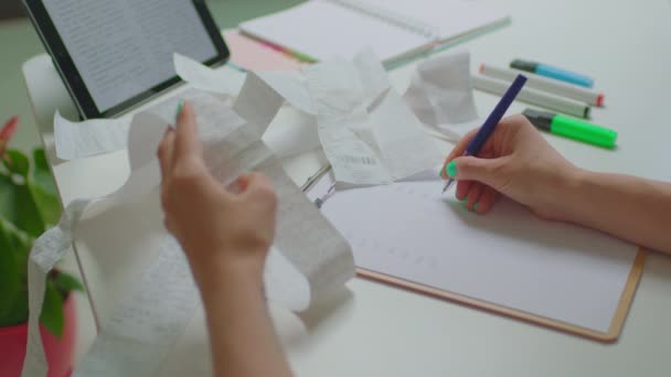 Vrouw die onkostenrekeningen onderzoekt en thuis op papier zit te schrijven. Huishoudbudgetbeheer. — Stockvideo