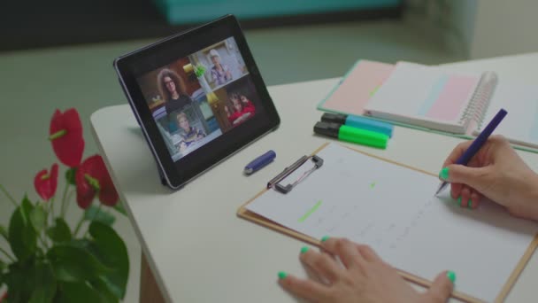 Profesoras escribiendo a mano en papel con estudiantes en línea hablando en tableta. Lección de escuela en línea en gadget. — Vídeo de stock