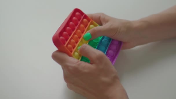 Mãos femininas brincando com o popular brinquedo anti-estresse de silicone pop-lo. Arco-íris simples jogo de covinhas poppit. — Vídeo de Stock