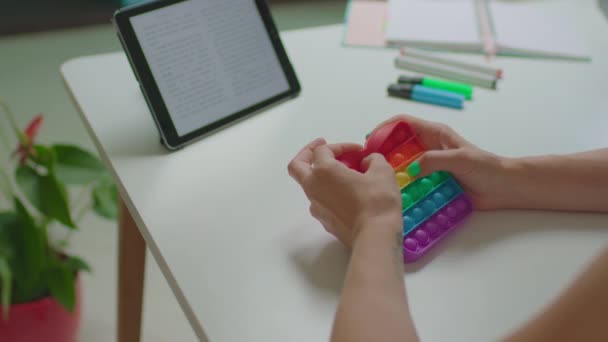 Vrouwelijke handen spelen met populaire siliconen anti-stress speelgoed pop het zittend op de werkplek met tablet computer. Rainbow eenvoudige kuiltje spel poppit voor ontspanning. — Stockvideo