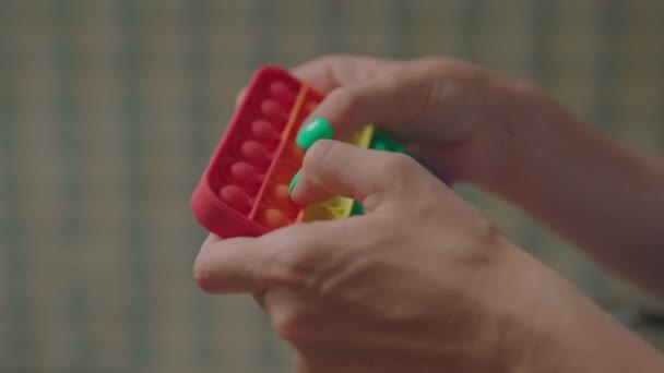 Mãos femininas brincando com o popular brinquedo anti-estresse de silicone pop-lo. Arco-íris simples jogo de covinhas poppit. — Vídeo de Stock