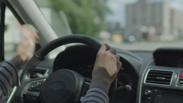 Zamknij żeńskie dłonie trzymając kierownicę podczas jazdy samochodem w mieście. Wnętrze pojazdu z kobietą kierowcą. Deska rozdzielcza samochodu. — Wideo stockowe